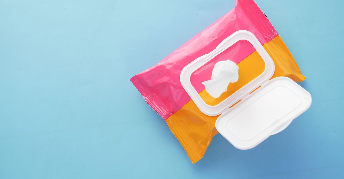 A pink and orange wet wipe pack lies open on a pale blue surface, its plastic flap lid raised.
