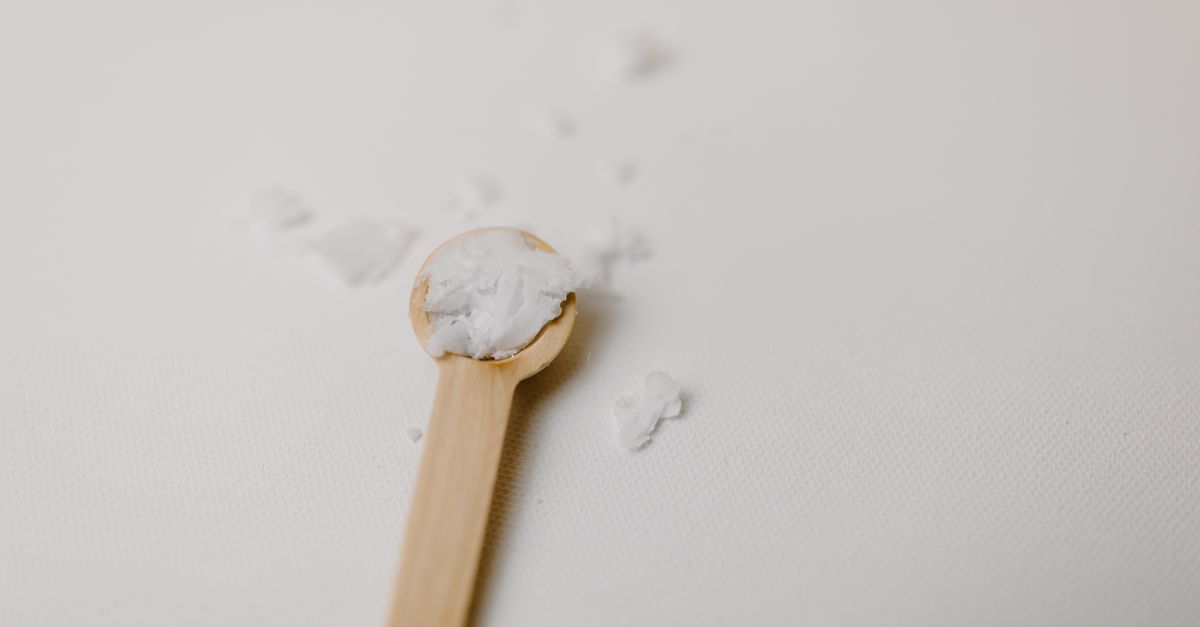A wooden spoon holds a small mound of white powder on a pale surface, a few grains scattered around it.