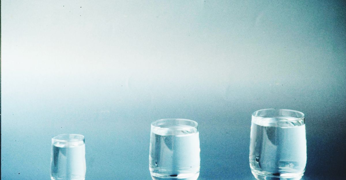 Three glasses of increasing size hold clear liquid at different levels, lit against a pale blue green wall.