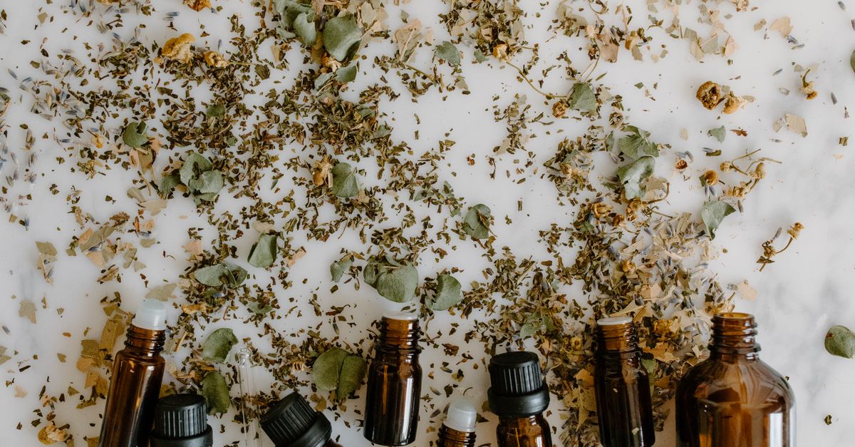Dried herb leaves are scattered across a white surface with a row of small dark glass bottles along the bottom edge.