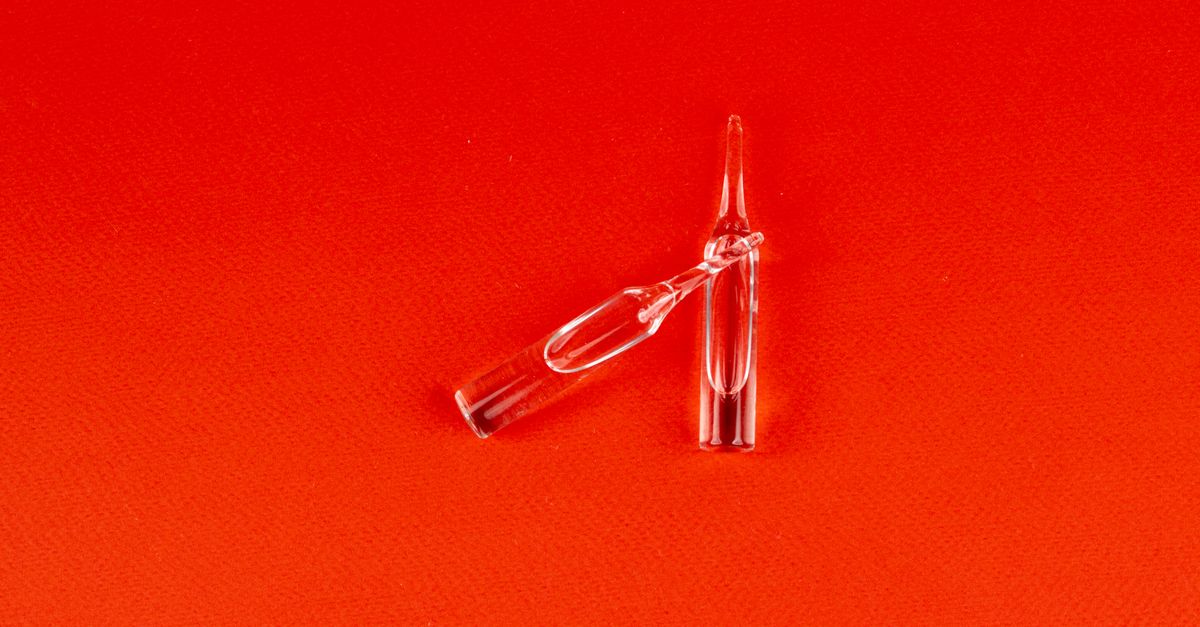 Two small clear glass ampoules lie on a bright red ground, one tipped over and one upright.