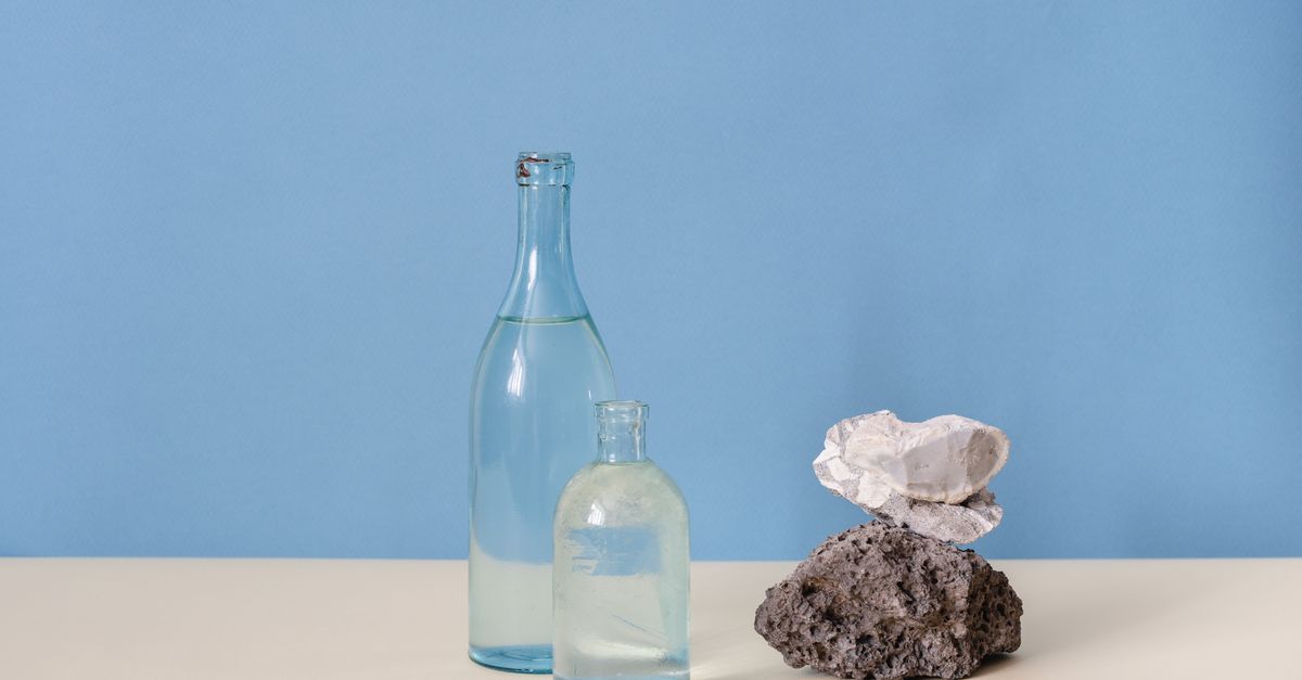 Two clear glass bottles and a smooth stone arranged on a pale surface.