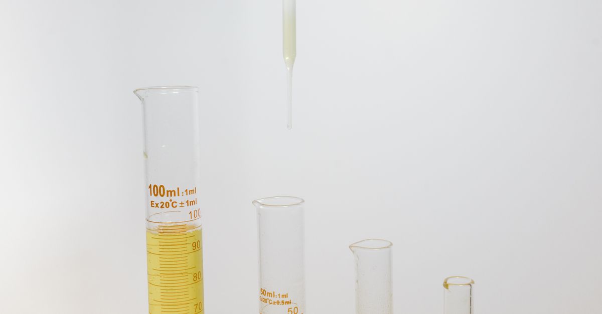 A graduated cylinder holds yellow liquid with a pipette poised above it, smaller empty cylinders standing to the side.