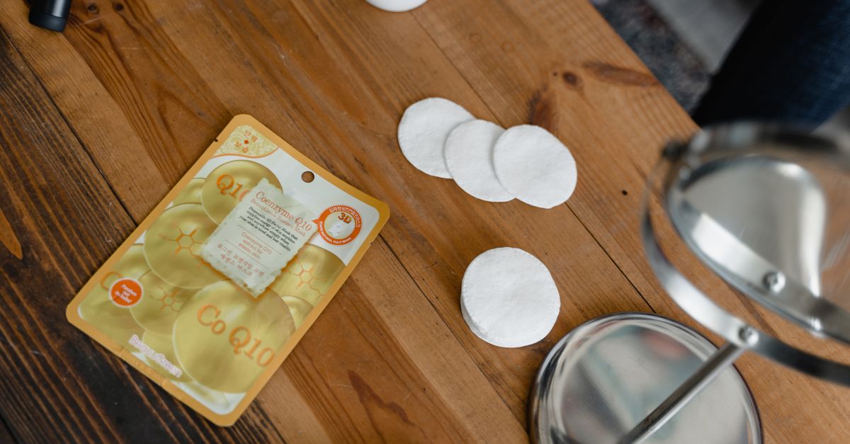 Cotton pads and unlabelled skincare bottles arranged on a wooden table.