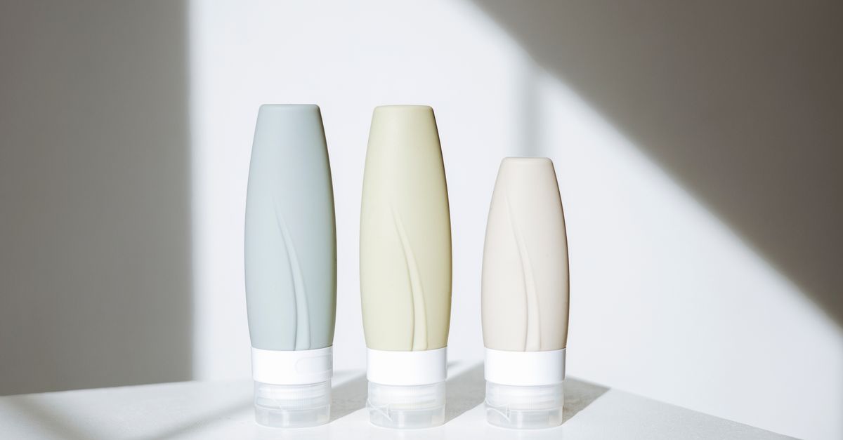 Three pastel squeeze bottles in grey blue, cream and beige stand together in a shaft of sunlight.