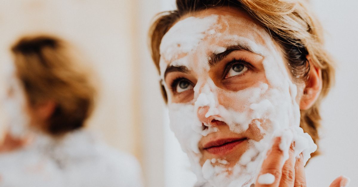 A person massaging white cleansing foam onto their face with both hands.