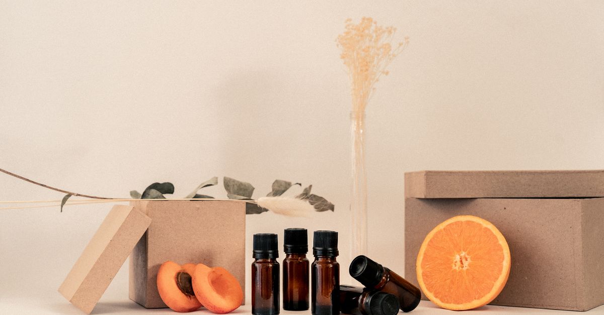 Small dark glass bottles stand among orange slices and kraft boxes with a dried sprig behind.