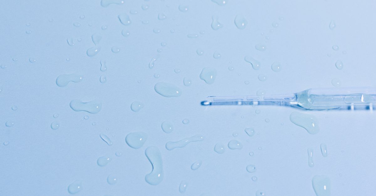 A glass pipette lies on a wet surface surrounded by scattered water droplets.