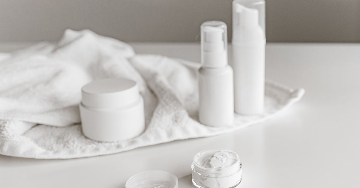 White jars and pump bottles are grouped on and around a folded white towel.