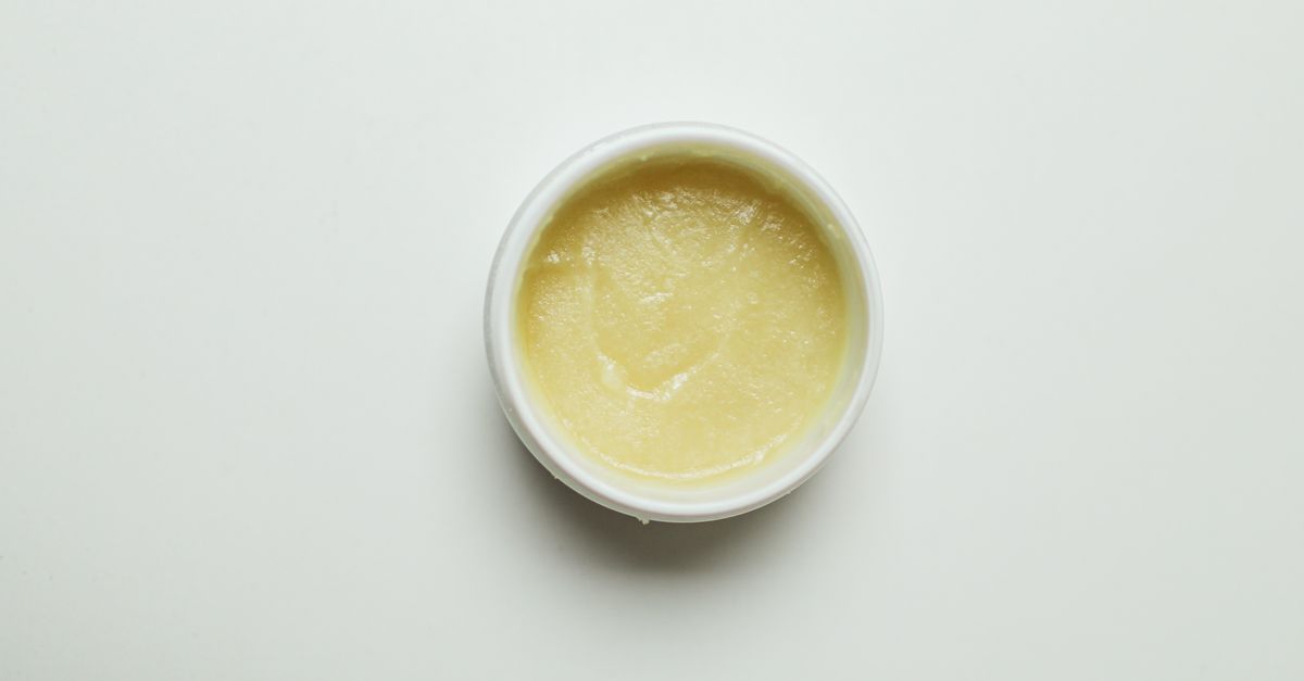 A small open white tub of pale yellow cream sits alone on a white surface.
