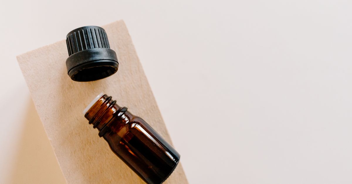 A small amber bottle lies on a kraft card with its black cap set beside it.