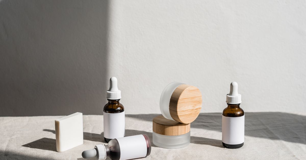 Dropper bottles, a jar with a bamboo lid and a square bar are arranged in a row along a pale ledge.