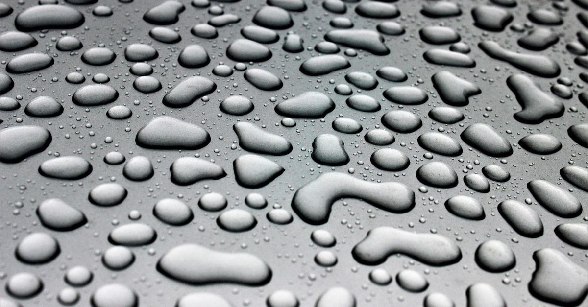Water beads of many sizes cover a flat grey surface.