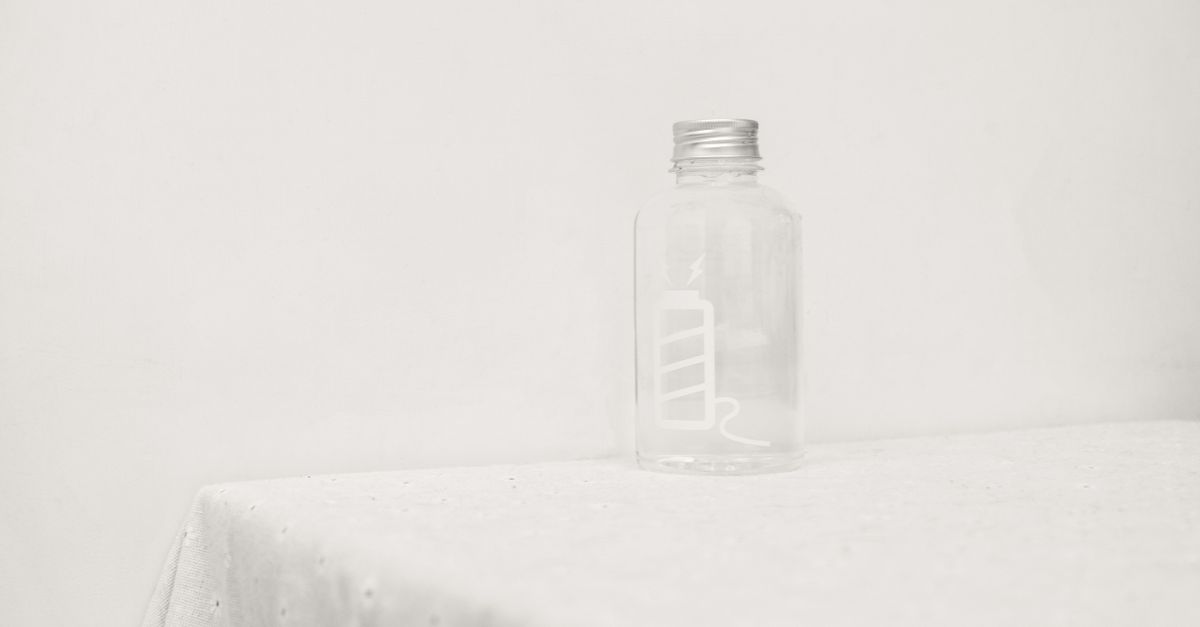 A single empty clear glass bottle stands on a white cloth in an otherwise bare frame.