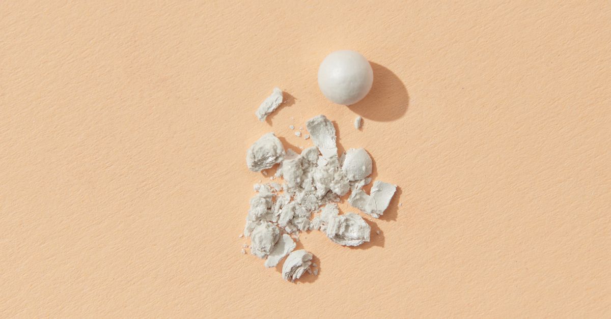Crumbled white powder and a single round bead lie on a peach coloured surface.