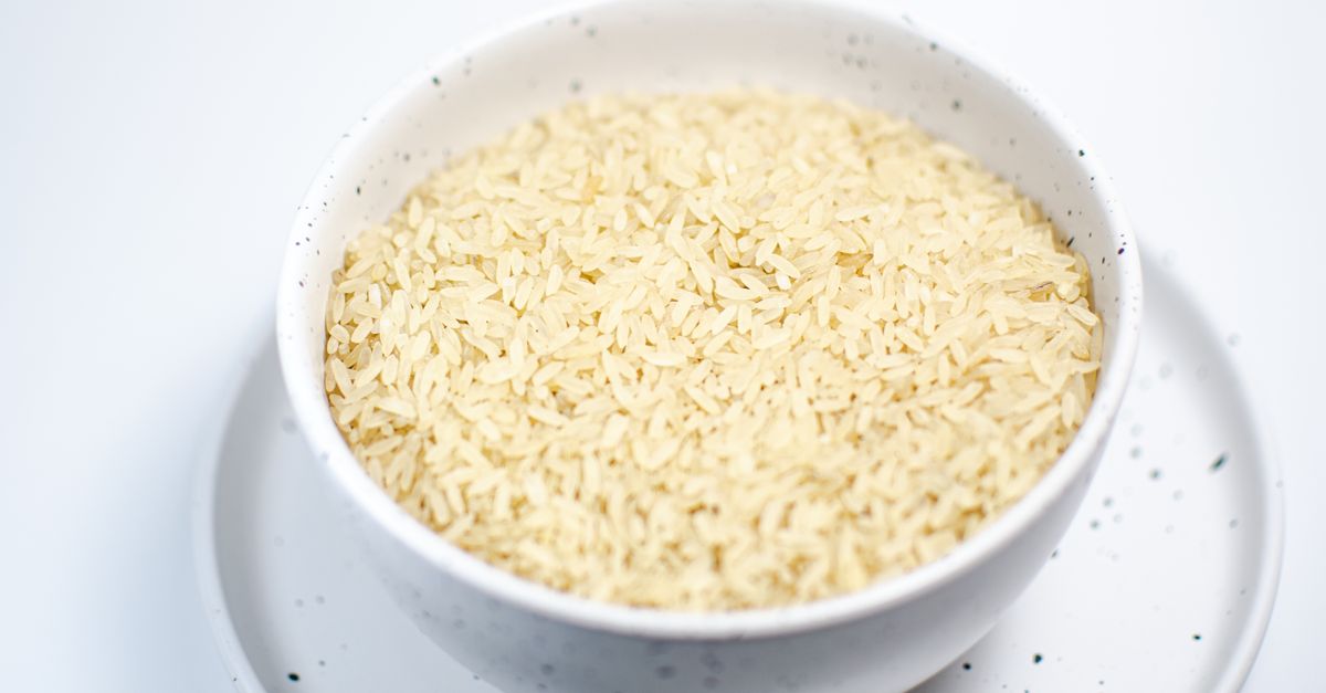 A white bowl heaped with uncooked rice sits on a matching plate.