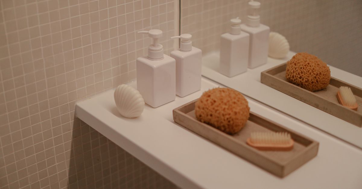 Pale pump bottles and natural sponges are arranged on tiled bathroom ledges.