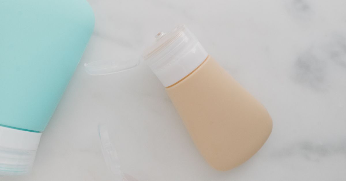 A mint green tube and a nude coloured tube lie together on a marble surface.