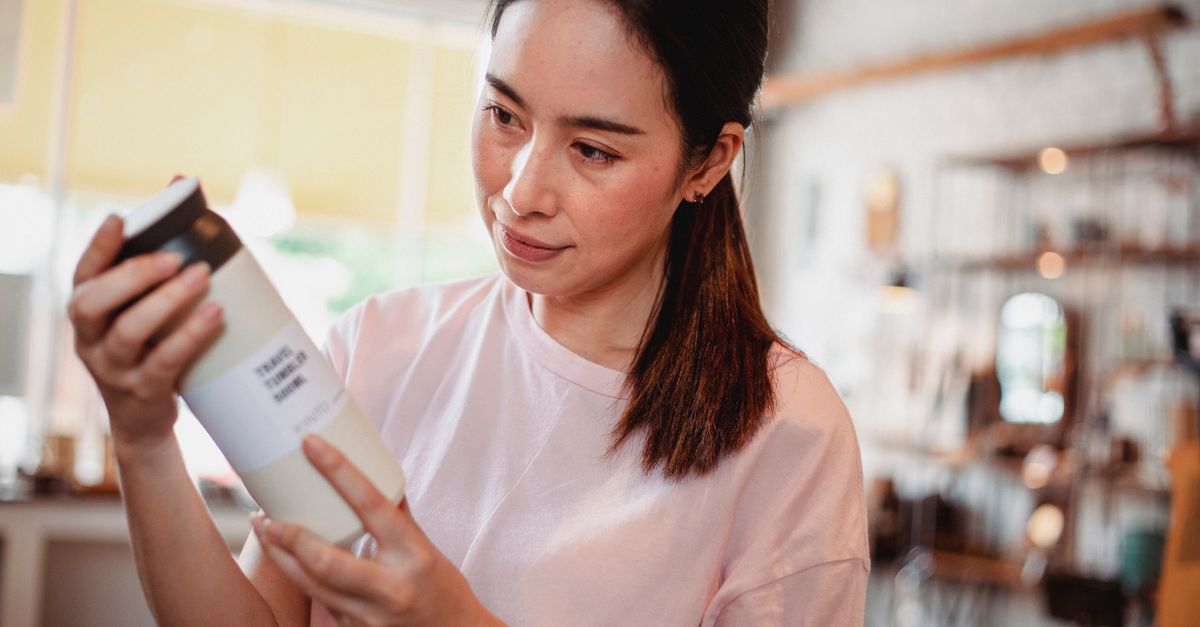 A shopper in a store holding a cosmetic bottle and reading the back of it.